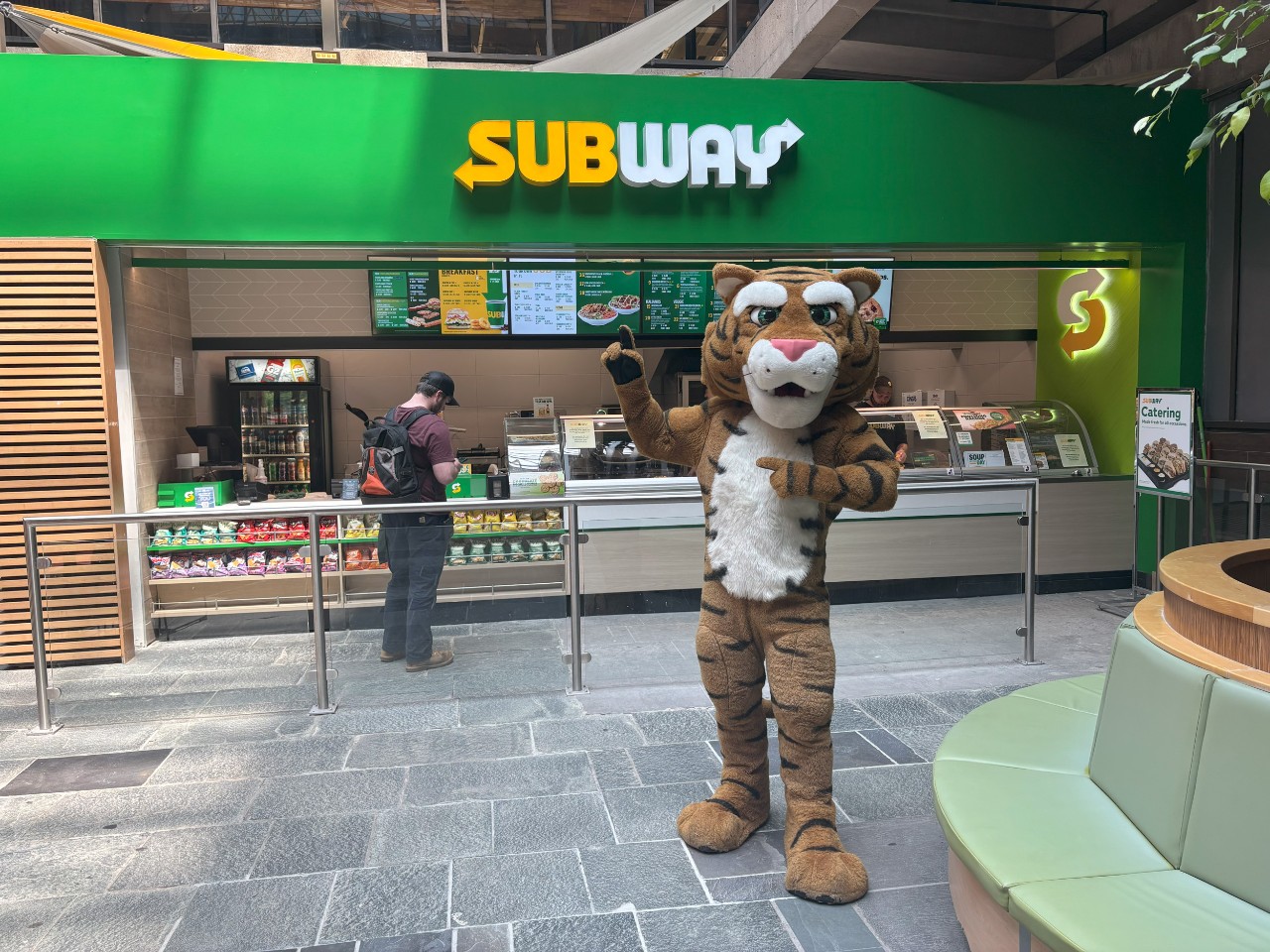 The Dal Tiger stands in front of the Subway in the Killam, pointing at the sign