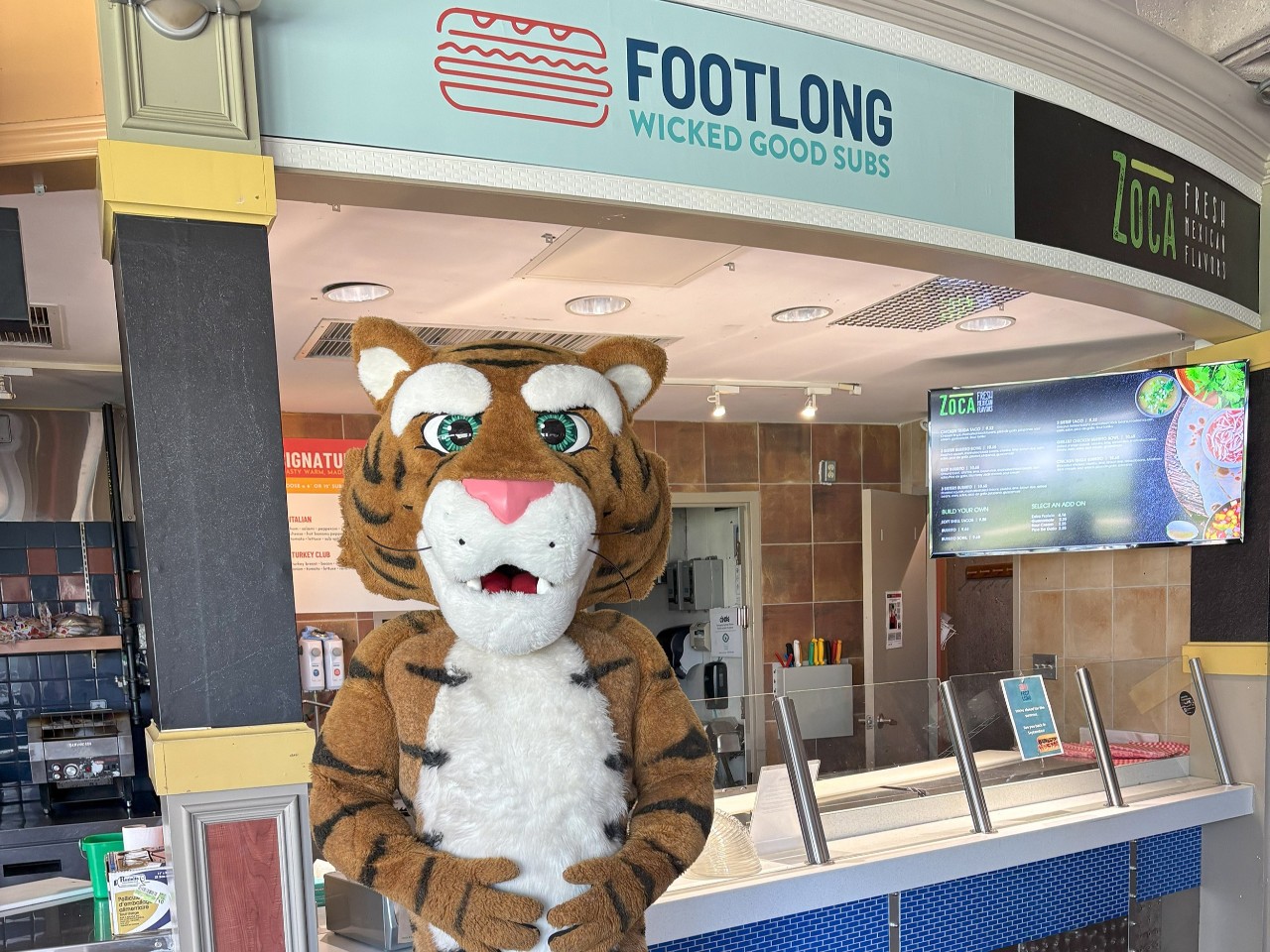 The Dal Tiger stands in front of the Footlong restaurant in the LSC with their hands on their tummy