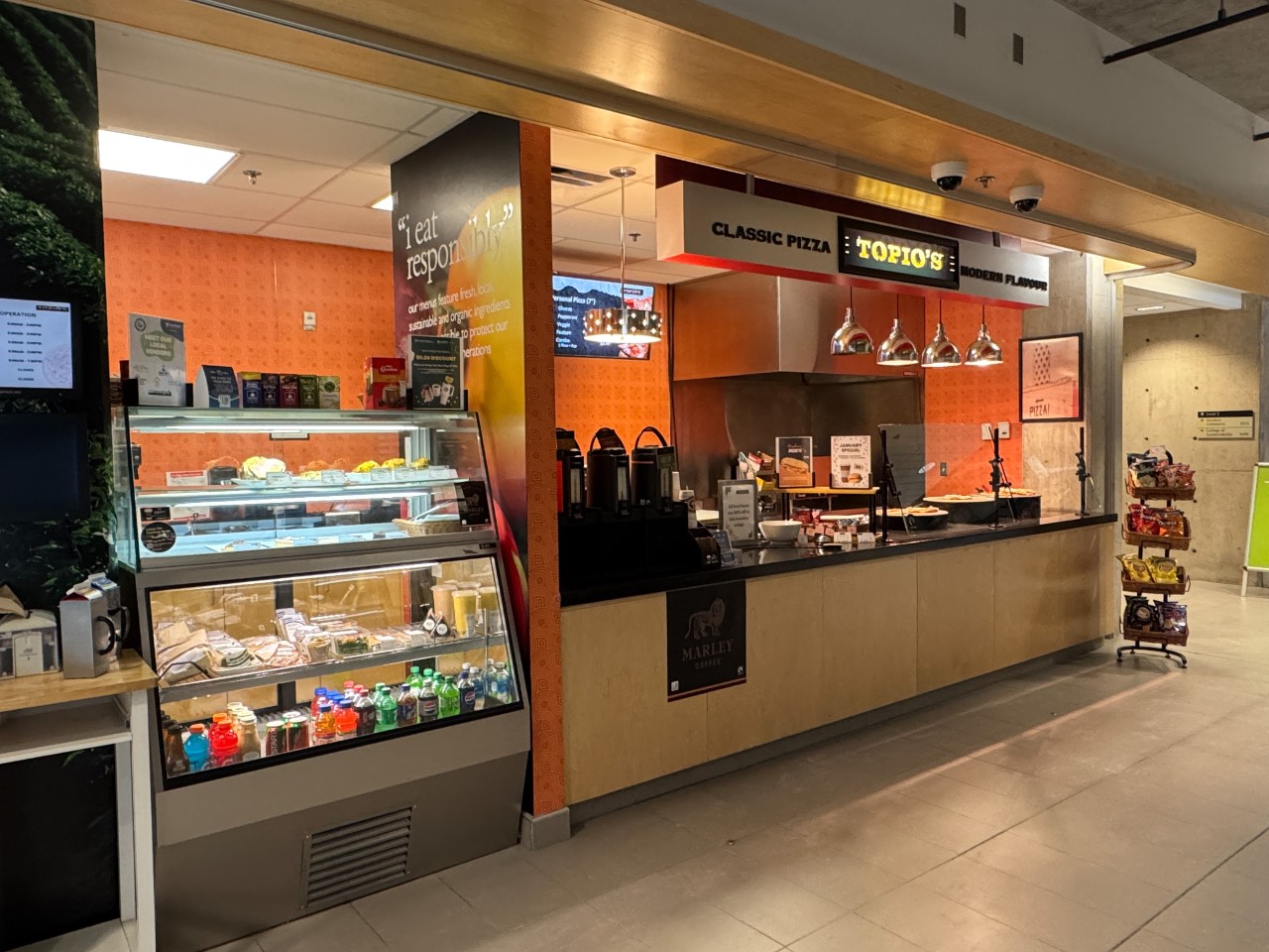 Topios in the Mona Campbell has a glass case of snack and lunch options, pizza stones, and coffee carafes along the counter.