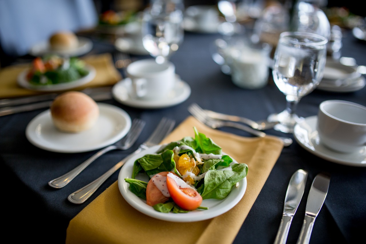 A plate of salad and a dinner roll sit on a dining table