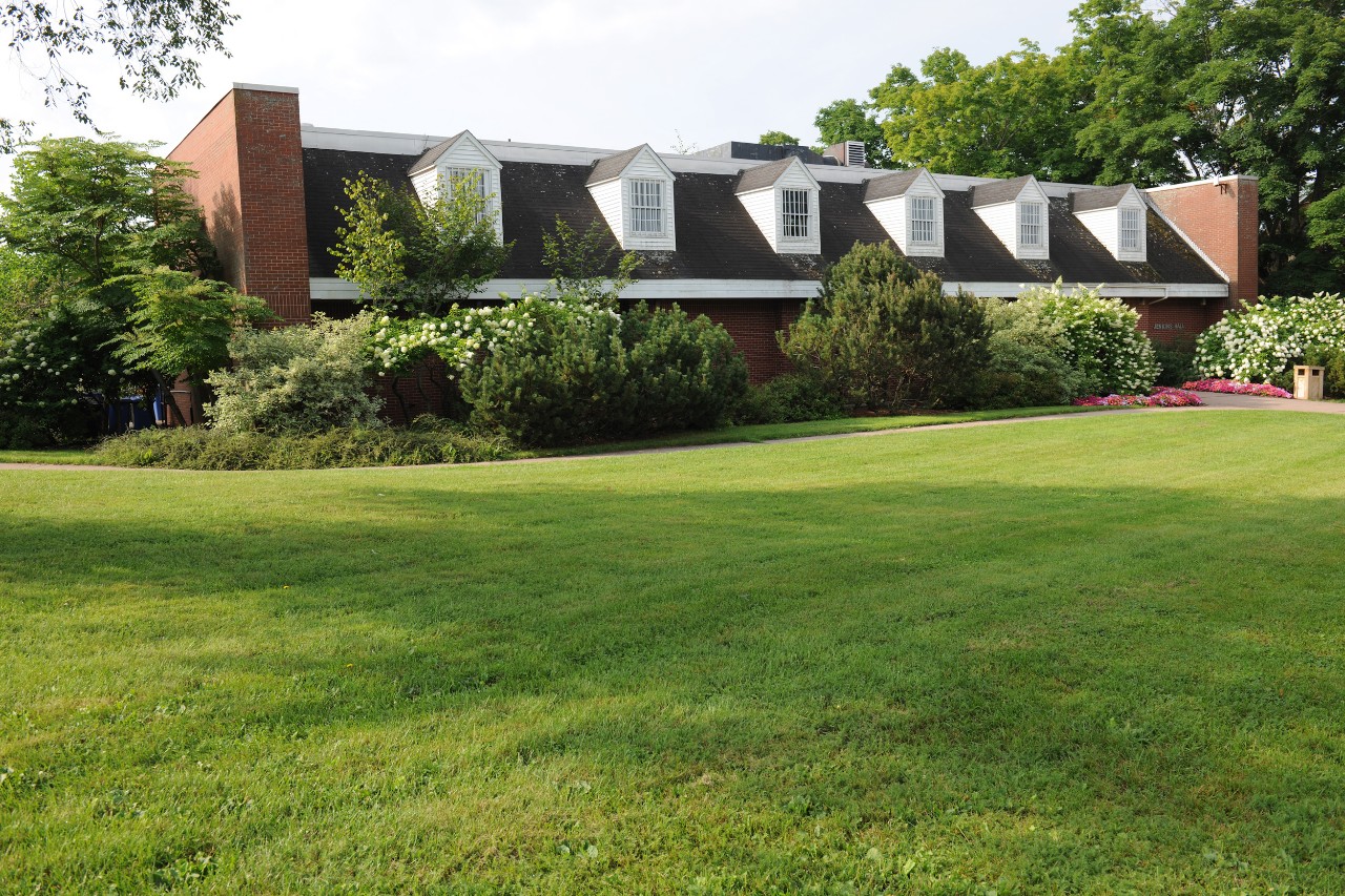 An exterior photo of the front entrance of Jenkins Hall, a low building with white dormers and bushes along the front