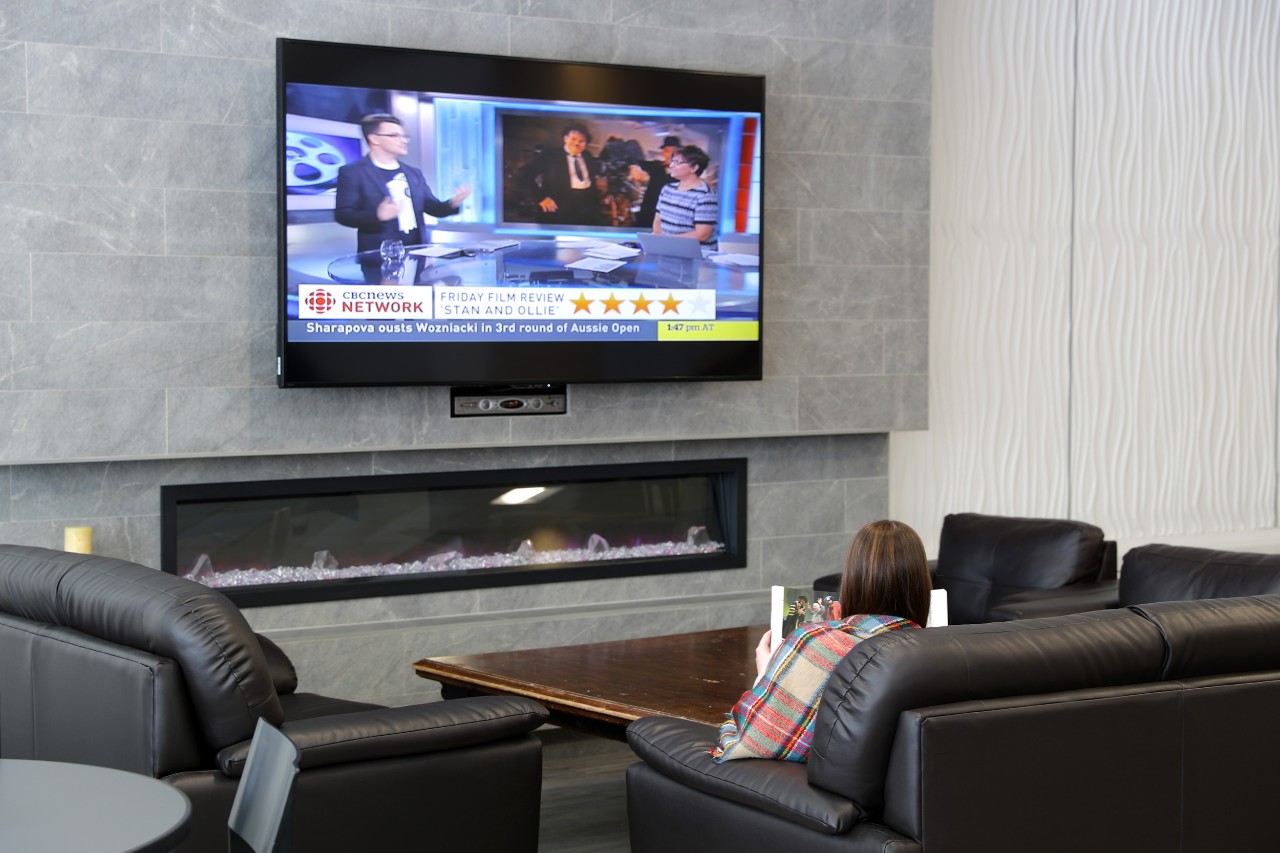 A student sits on a leather sofa in front of a large TV over an electric fireplace