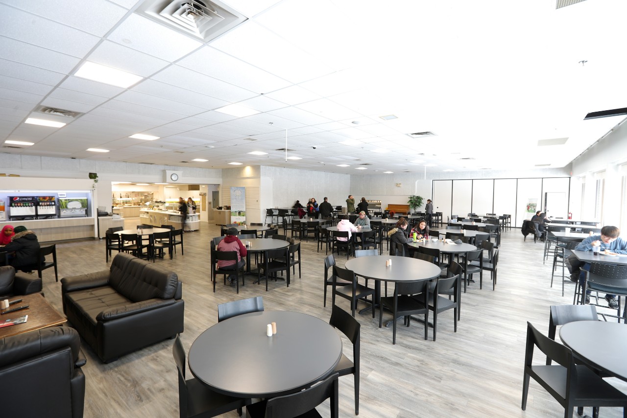 A wide photo of the seating area at Jenkins Hall shows the sofas and many round tables in the  bright, open space