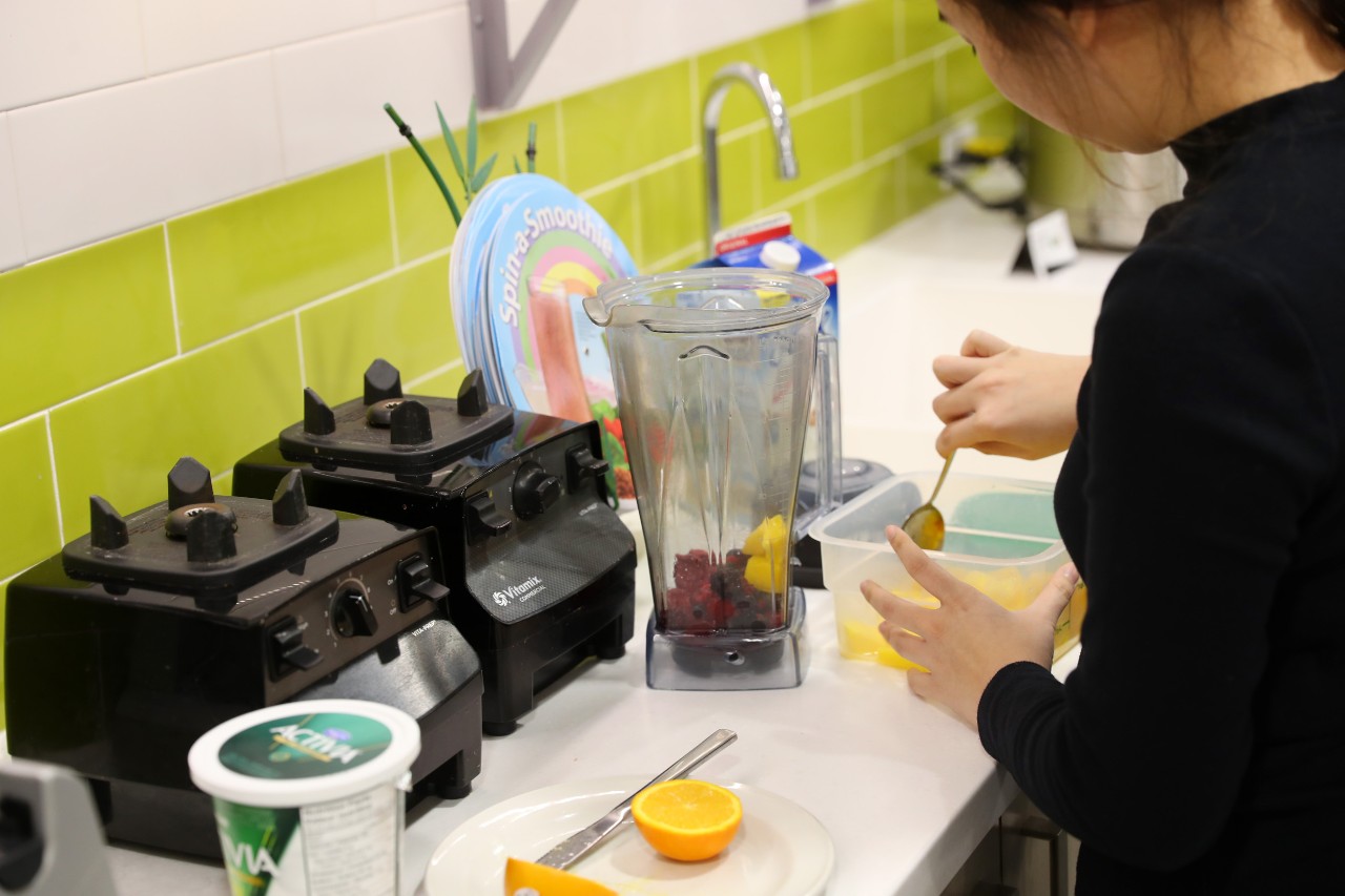 A student scoops ingredients into a blender to make a custom smoothie