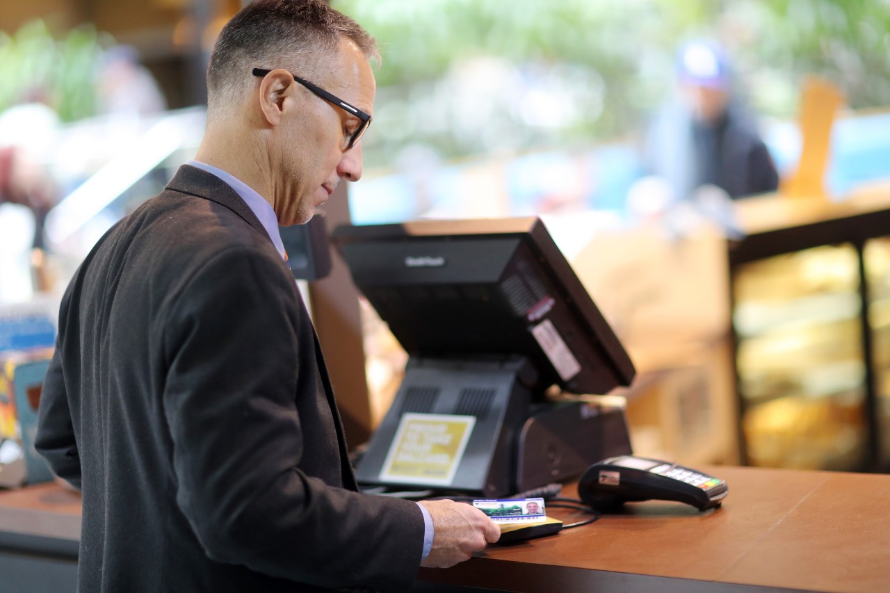 A male staff member with grey hair and glasses pays at a checkout with his DalCard