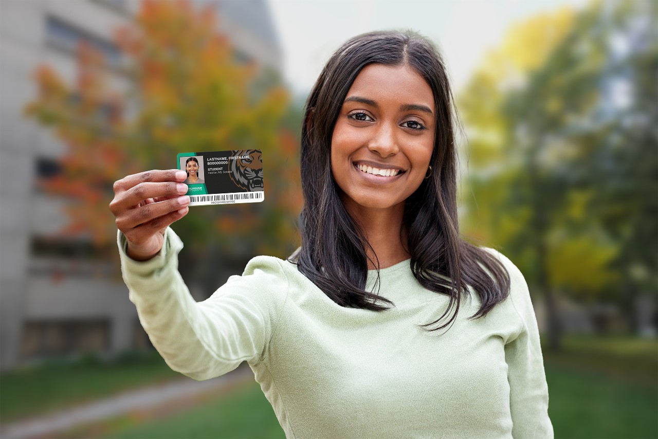 A young woman with brown skin and hair stands outdoors holding a DalCard up to the camera