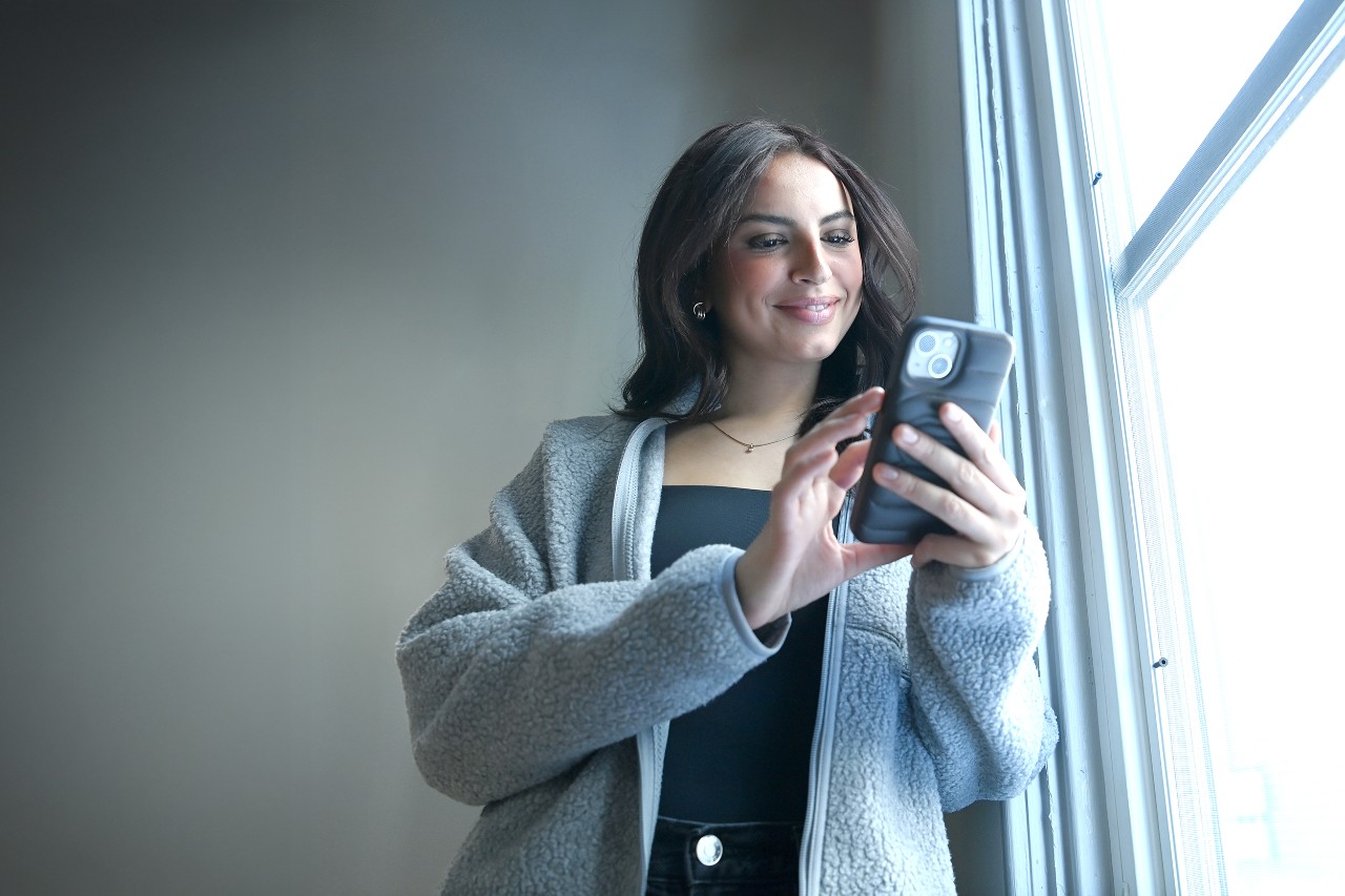 A young dark-haired woman smiles while looking at her phone