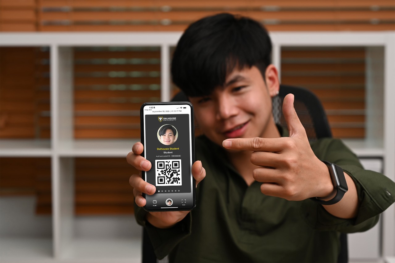 A male asian student holds up his phone to the camera with the DalCard mobile card on the screen