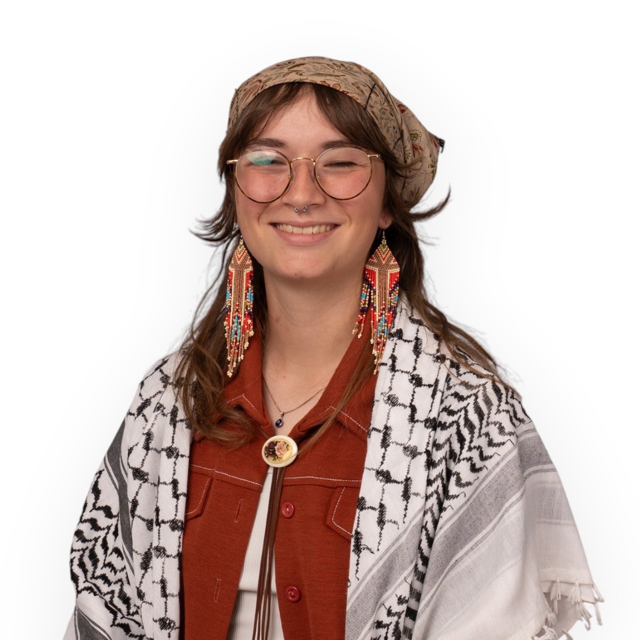 A portrait of Eve wearing glasses, head kerchief, long earrings, maroon top, and black and white shawl.