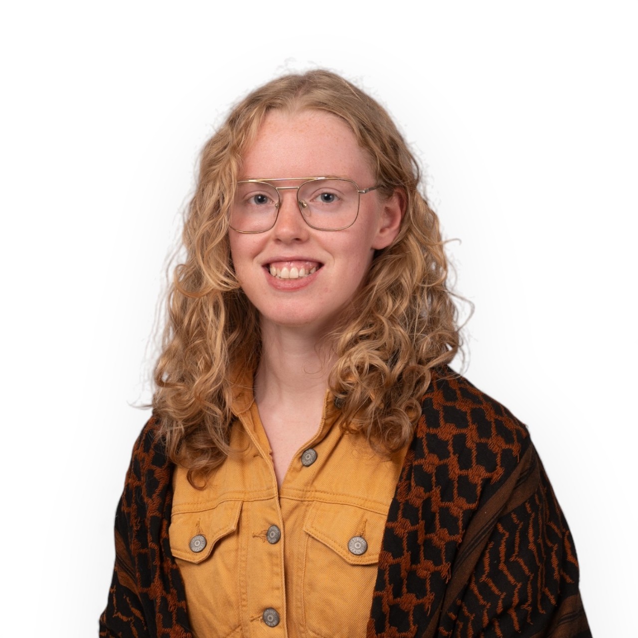 A portrait of Maren wearing glasses, a yellow top and black and red cardigan.