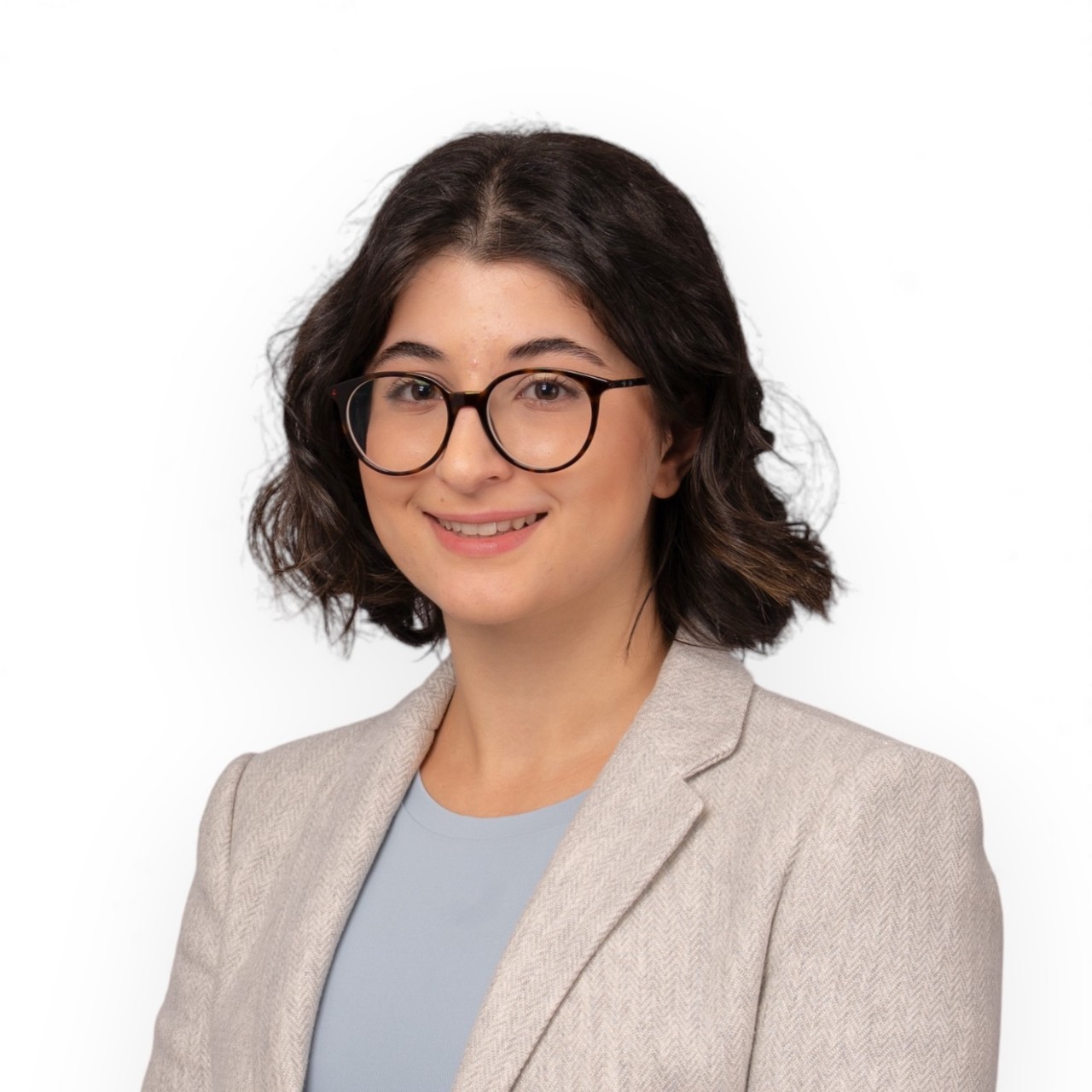 A portrait of Tatiana dressed in a beige blazer, light blue shirt, and glasses.