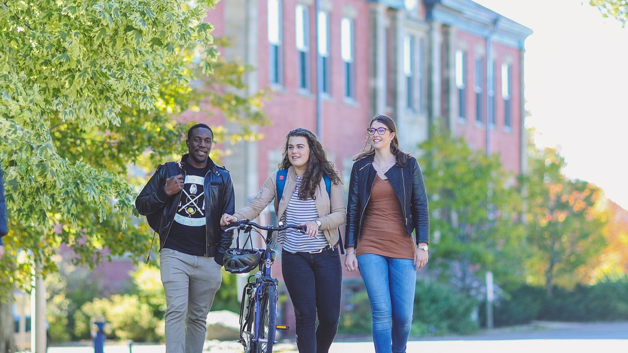 3 students walking on campus in front of Cumming Hall