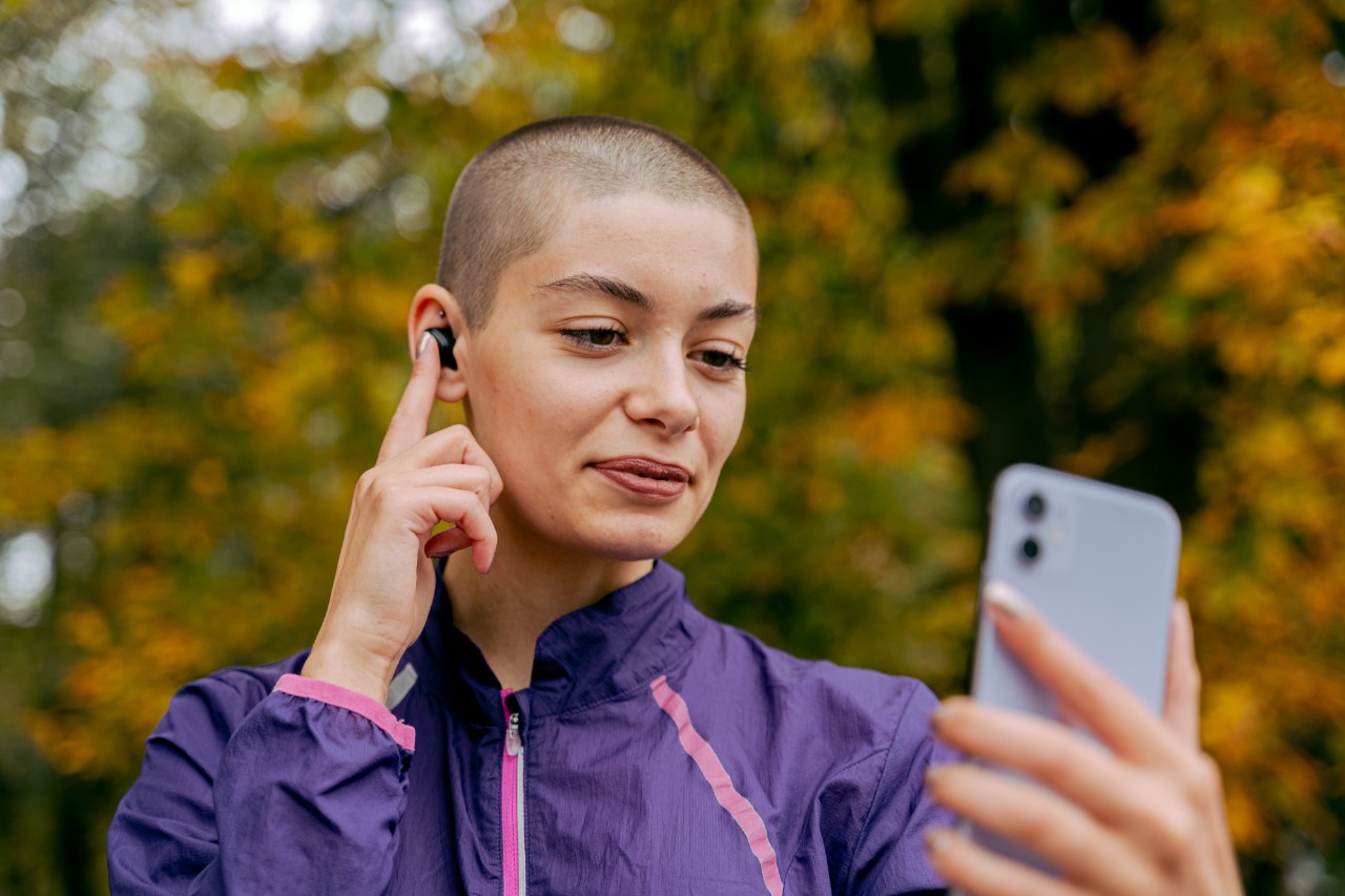 Student with an ear piece holding up and looking at mobile phone