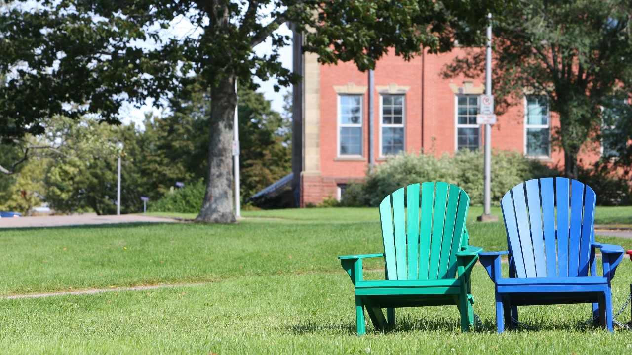 Two Adirondack-style chairs – one green and one blue – sit on the lawn at Dalhousie’s Agricultural Campus in Truro, adjacent to the residences. 