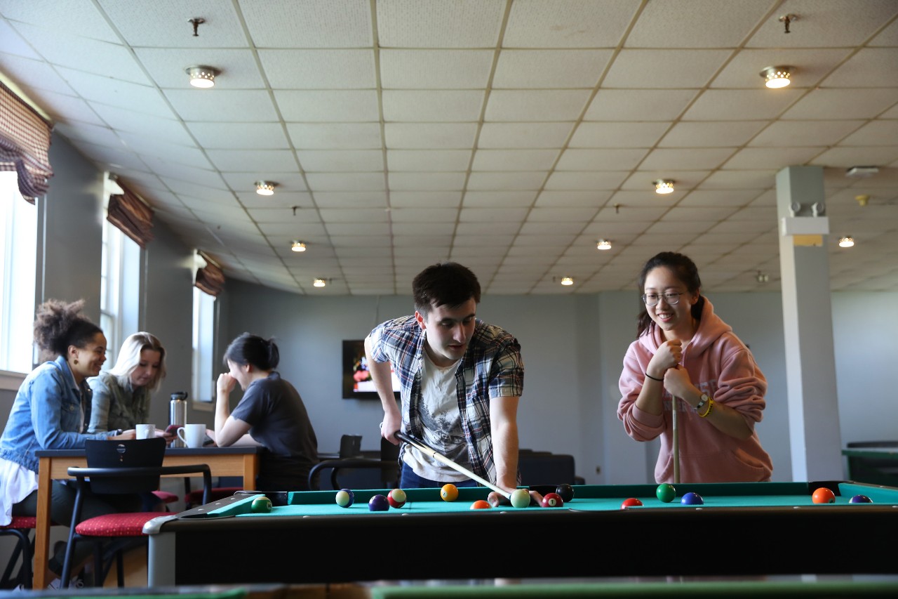 Summer residents play pool in a lounge on the Truro campus