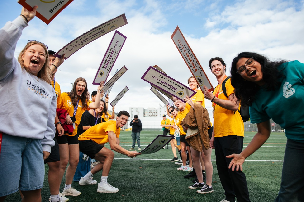 Members of the residence life team hold signs for buildings and houses on Wickwire Field, welcoming residents
