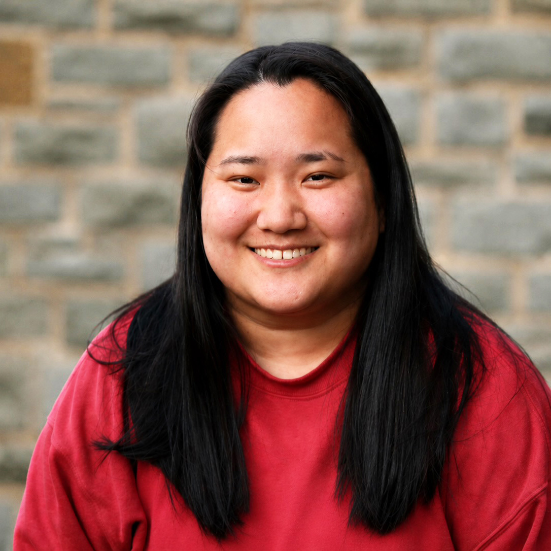 A portrait of a smiling young woman of asian descent with straight dark hair and a red long-sleeved shirt.