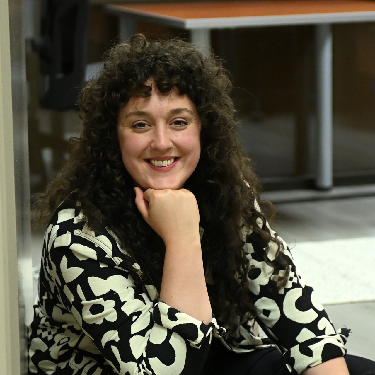 A portrait of Olivia Fader - a young woman with dark curly hair smiling at the camera