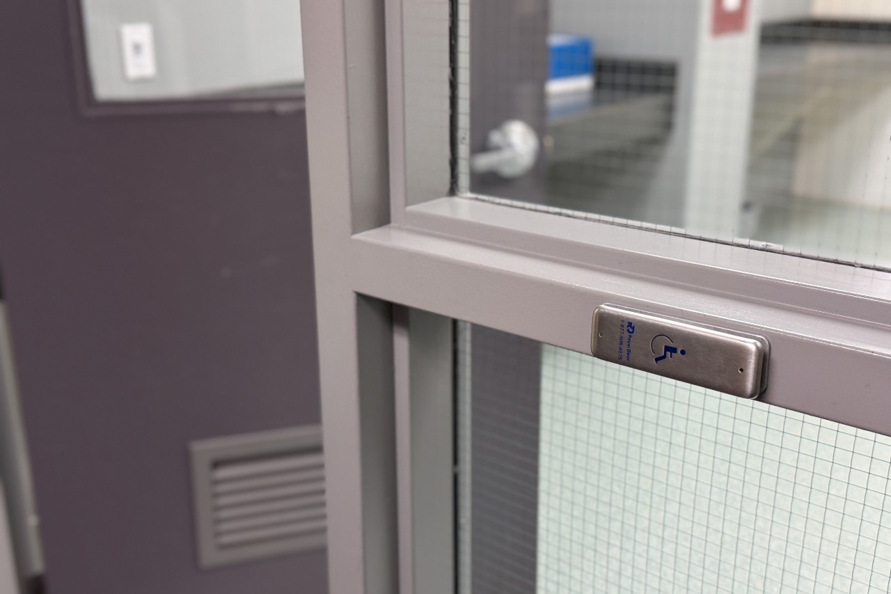 Close up photo of an automatic door opener button in the hallway of a residence, next to an open door. 