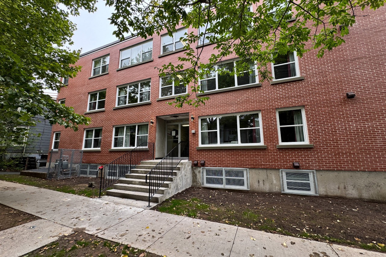 The front entrance of Glengary Apartments, a converted low-rise apartment building. The exterior is red brick and there are plenty of green trees along the sidewalk