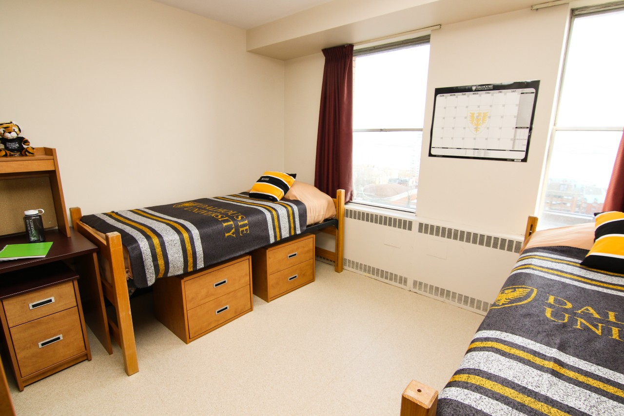A double room in Gerard Hall with 2 beds, storage, desk, and 2 large windows