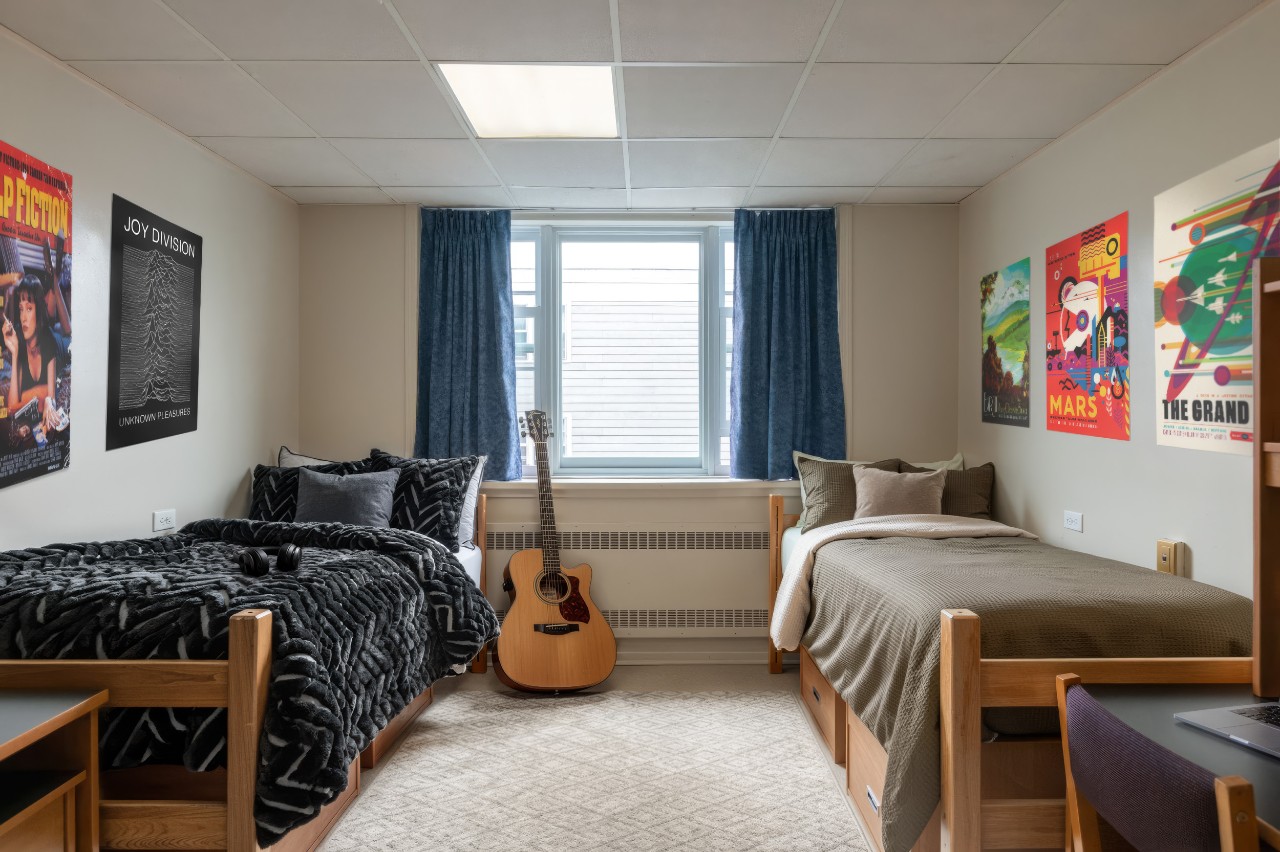 A double room in Henderson House in Howe Hall, staged with bedding, a laptop on the desk, and posters on the wall.