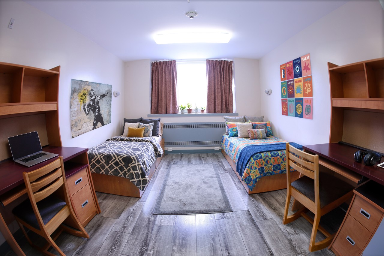 A double room in Cameron House in Howe Hall, staged with bedding, a laptop on the desk, and posters on the wall.