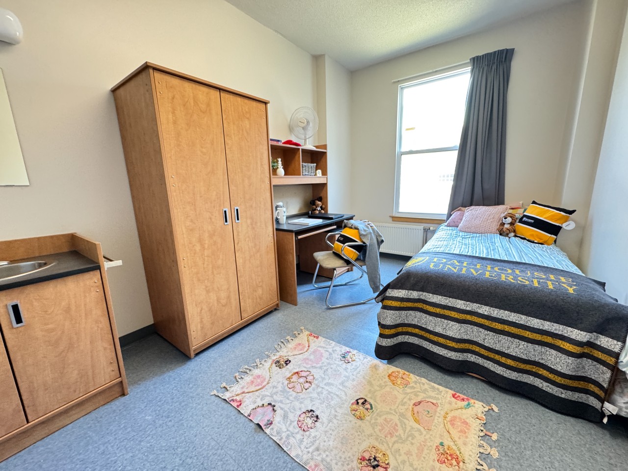A single room in Fountain House with a bed, desk, wardrobe and sink