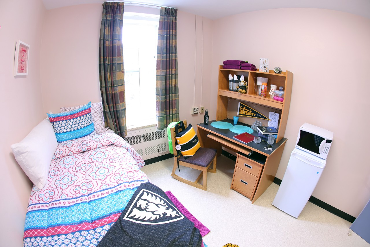 A single room in Smith House with a colourful bedspread, desk, mini fridge, and decorative items