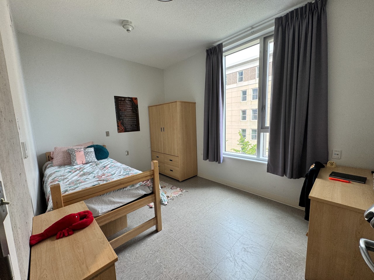 A bedroom in a 3-bedroom suite in LeMarchant Place featuring a bed, desk, wardrobe, and shelves.