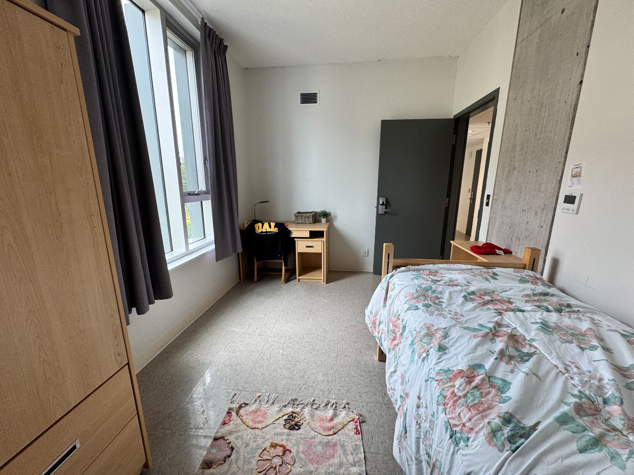 A bedroom in a 3-bedroom suite in LeMarchant Place featuring a bed, desk, wardrobe, and shelves.