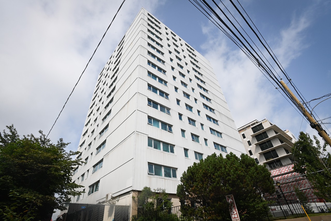Peter Green Hall is a tall apartment building, clad in grey siding, ascending skyward behind trees