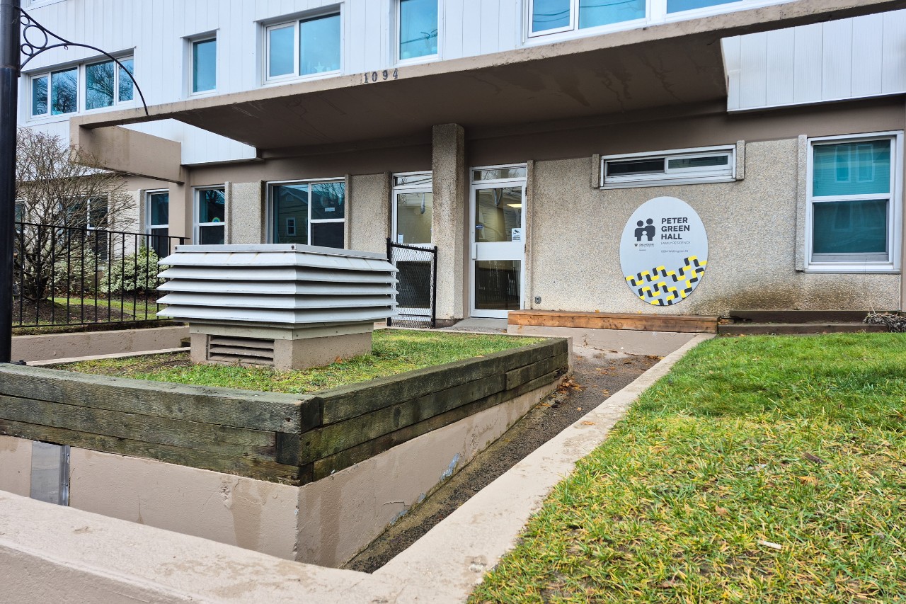 The front entrance to Peter Green Hall - with glass doors and a metal sign on the concrete exterior