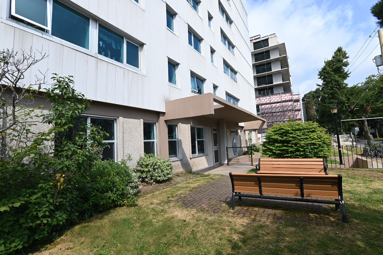 The shared courtyard near the front entrance has two park benches and several bushes and shrubs along the brick walkway