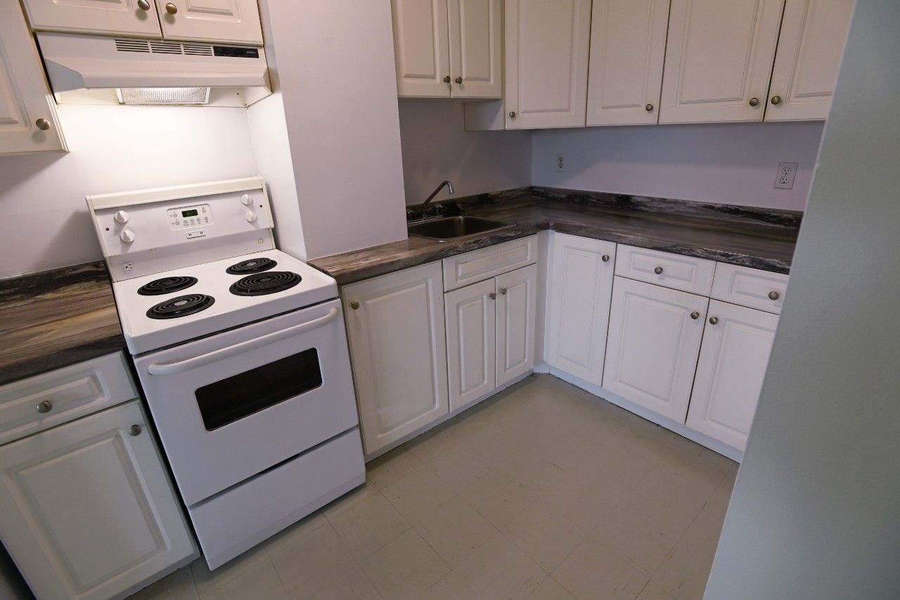 The full kitchen in a one-bedroom unit with white cupboards and appliances
