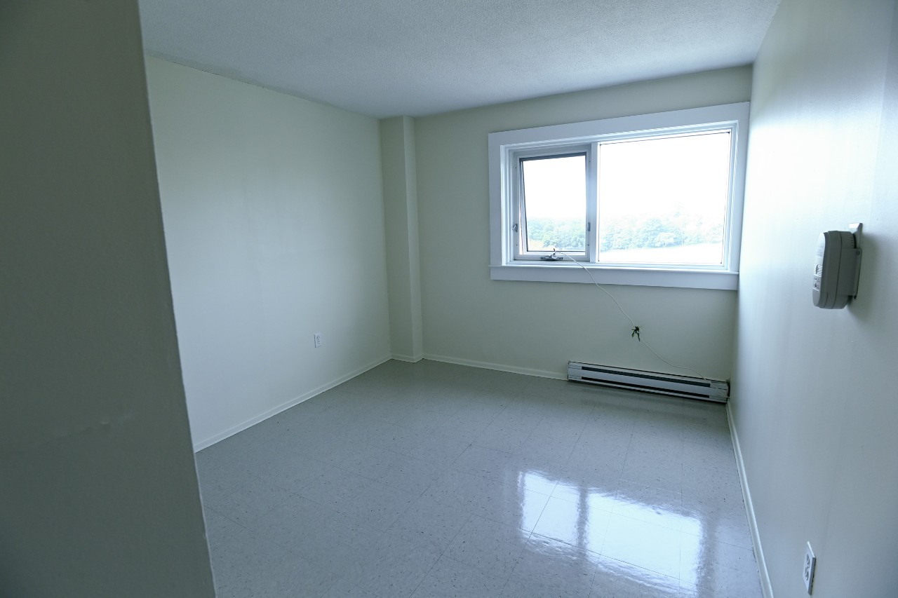 The bedroom of a one-bedroom unit with a large window and glossy linoleum floors