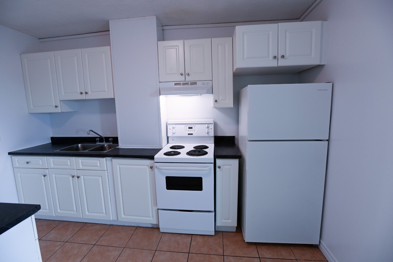 The full kitchen in a two-bedroom unit, with white appliances and cupboards and light brown tile floor