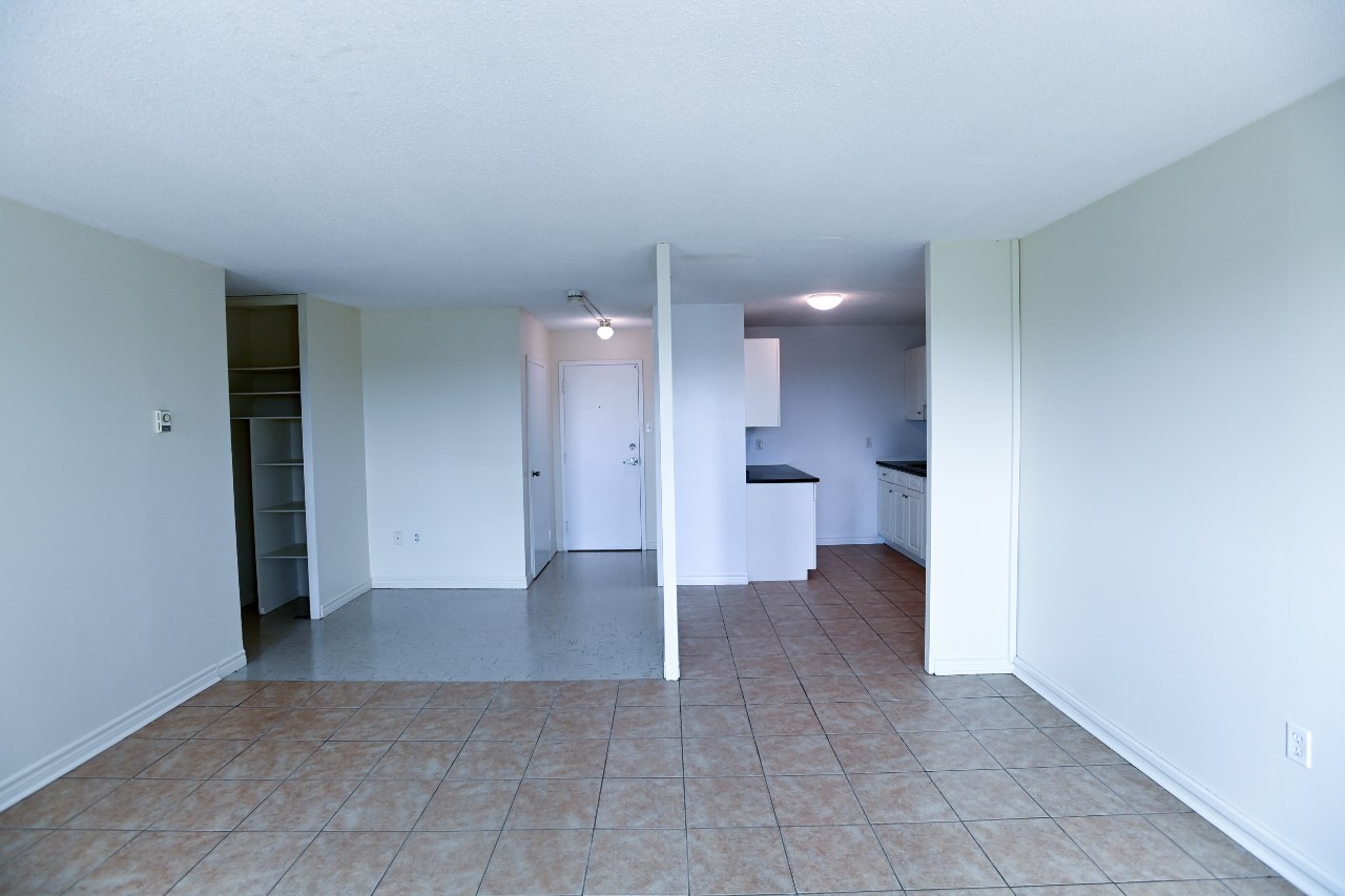 The view from the living room to the kitchen, front entrance, and bedroom hallway