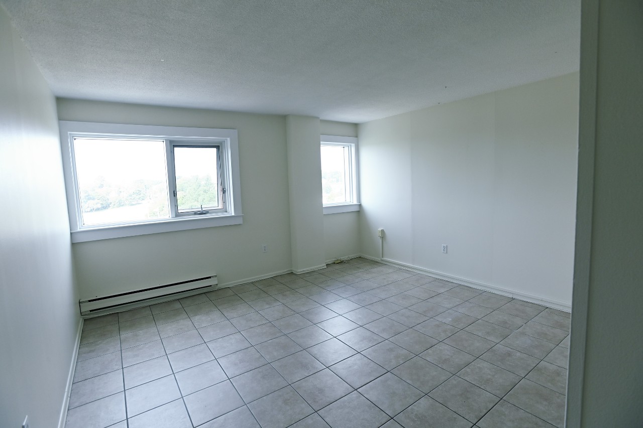 The large living room in a one-bedroom unit has tile floors and large windows with plenty of natural light
