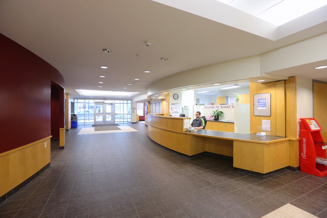 The Risley Hall lobby, bustling with students, with the washrooms and dining hall on the left and front desk on the right, looking toward the front door.