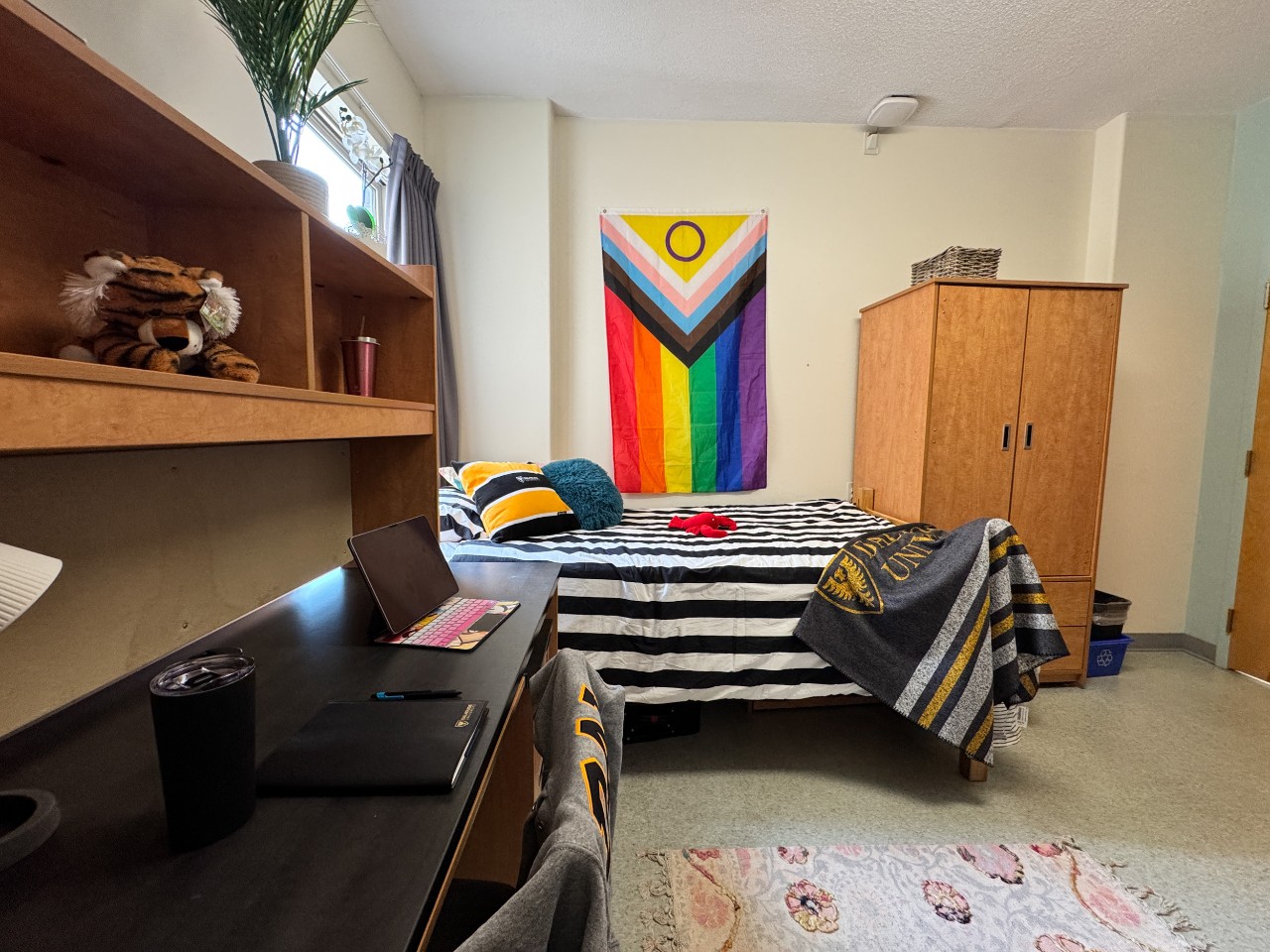 One side of a double room in Risley Hall, with a Dal blanket draped over the foot of the bed and a pride flag on the wall.