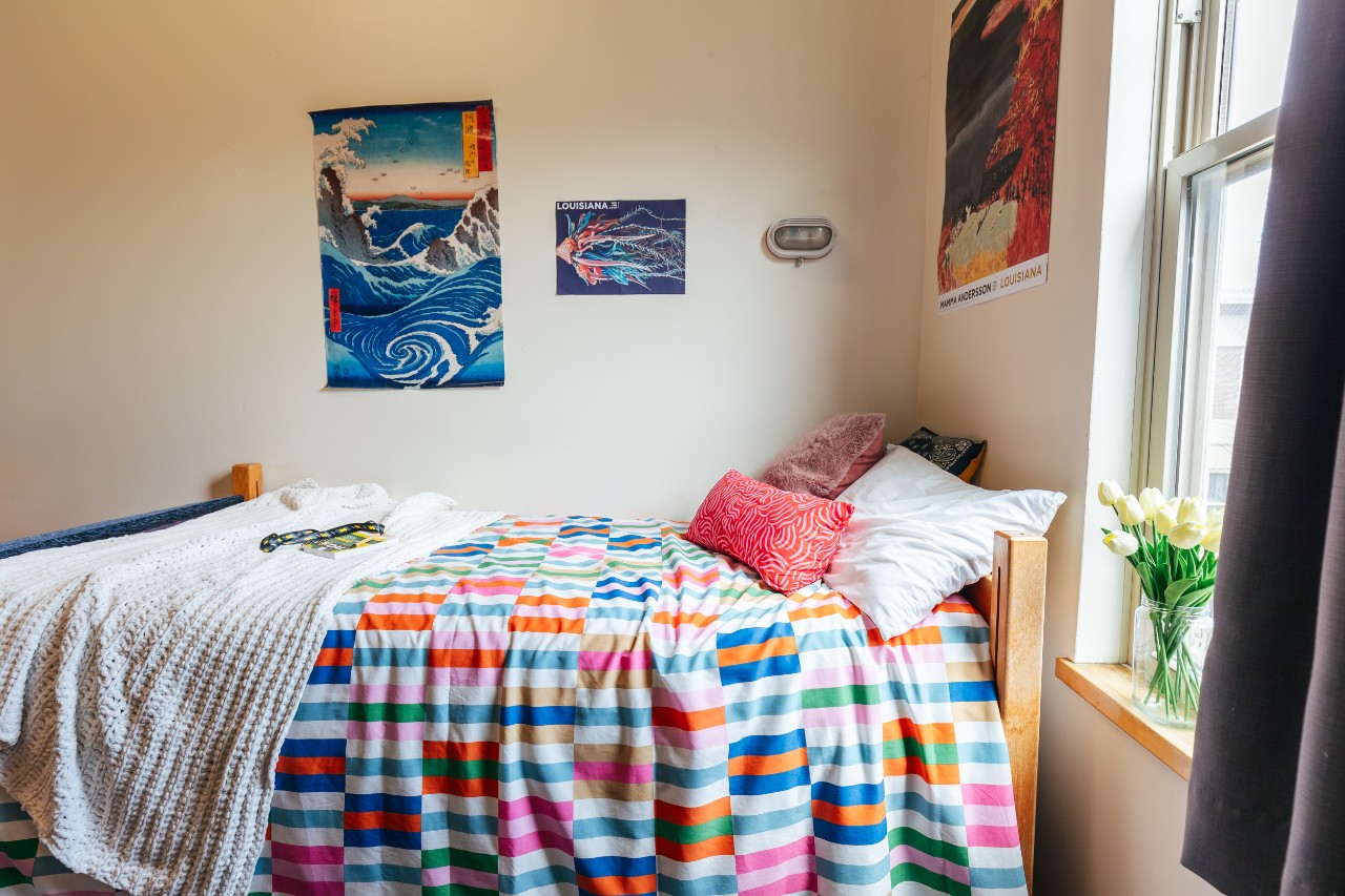 A bed in a single room in RIsley Hall, with a colourful blanket and posters on the wall.
