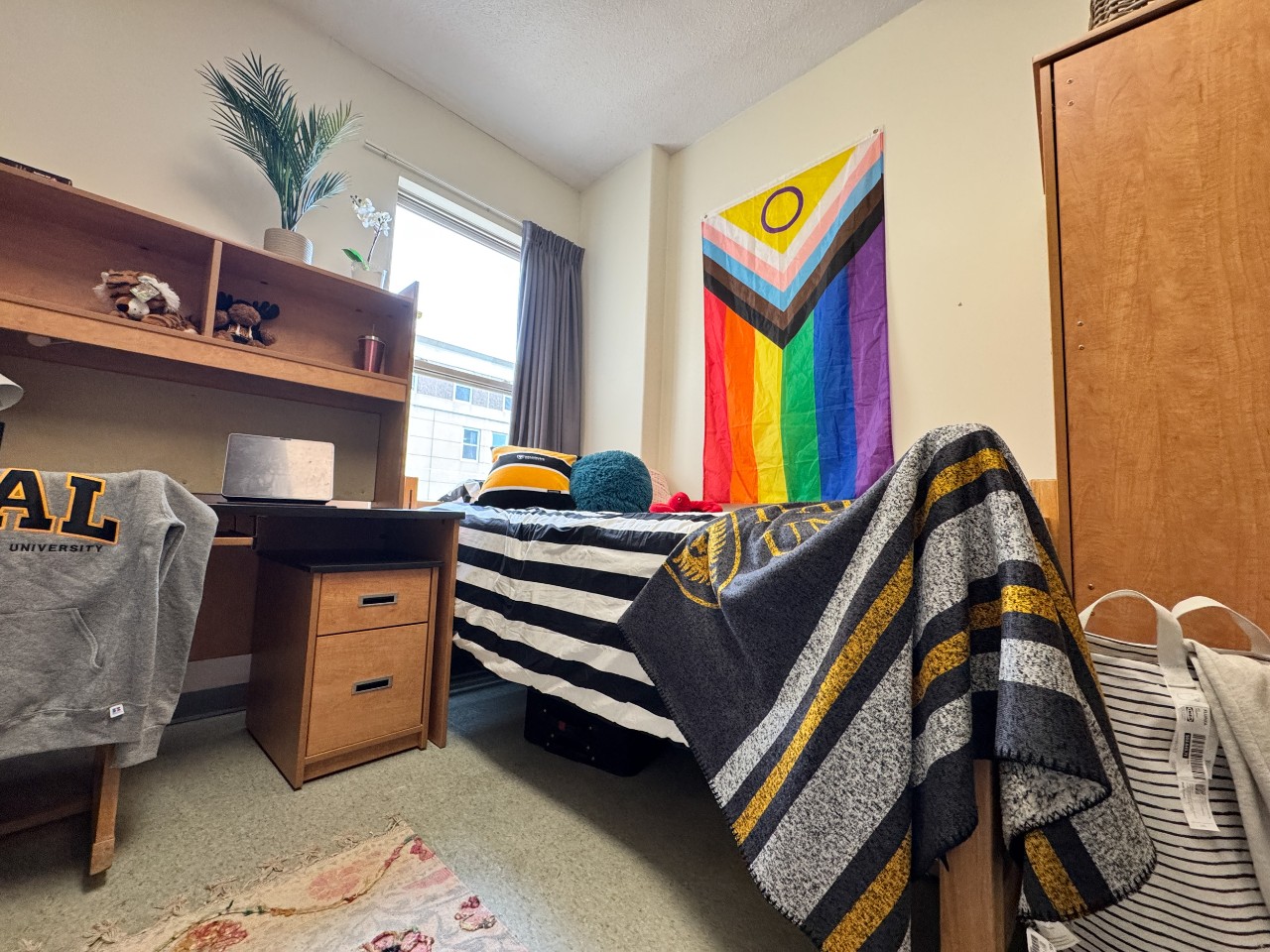 One side of a double room in Risley Hall, with a Dal blanket draped over the foot of the bed and a pride flag on the wall.