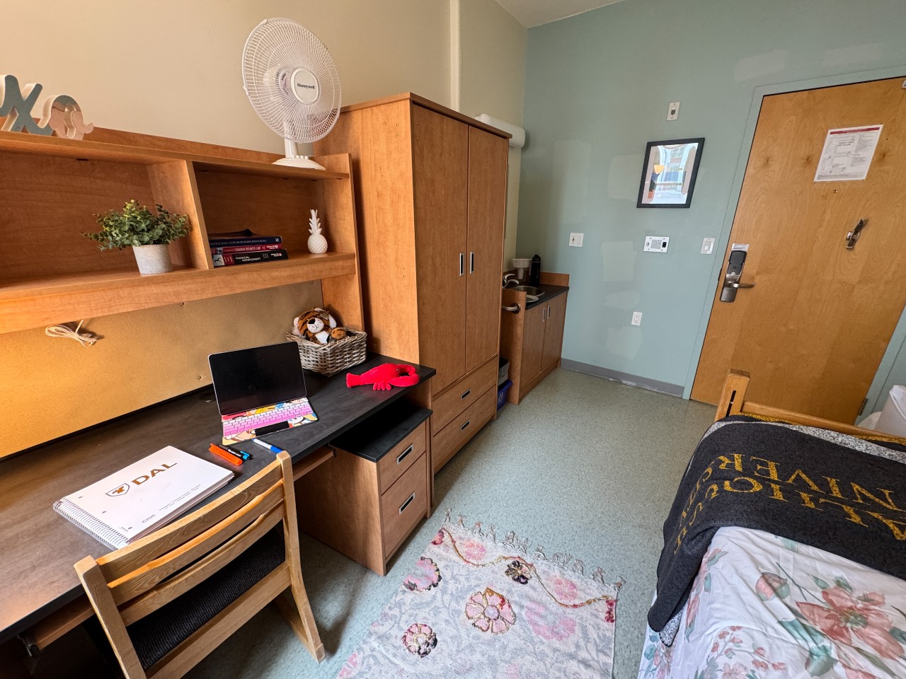 A single room in Risley Hall with an adjustable bed, desk, wardrobe, and a mini fridge. There is a sink in the corner near the door.