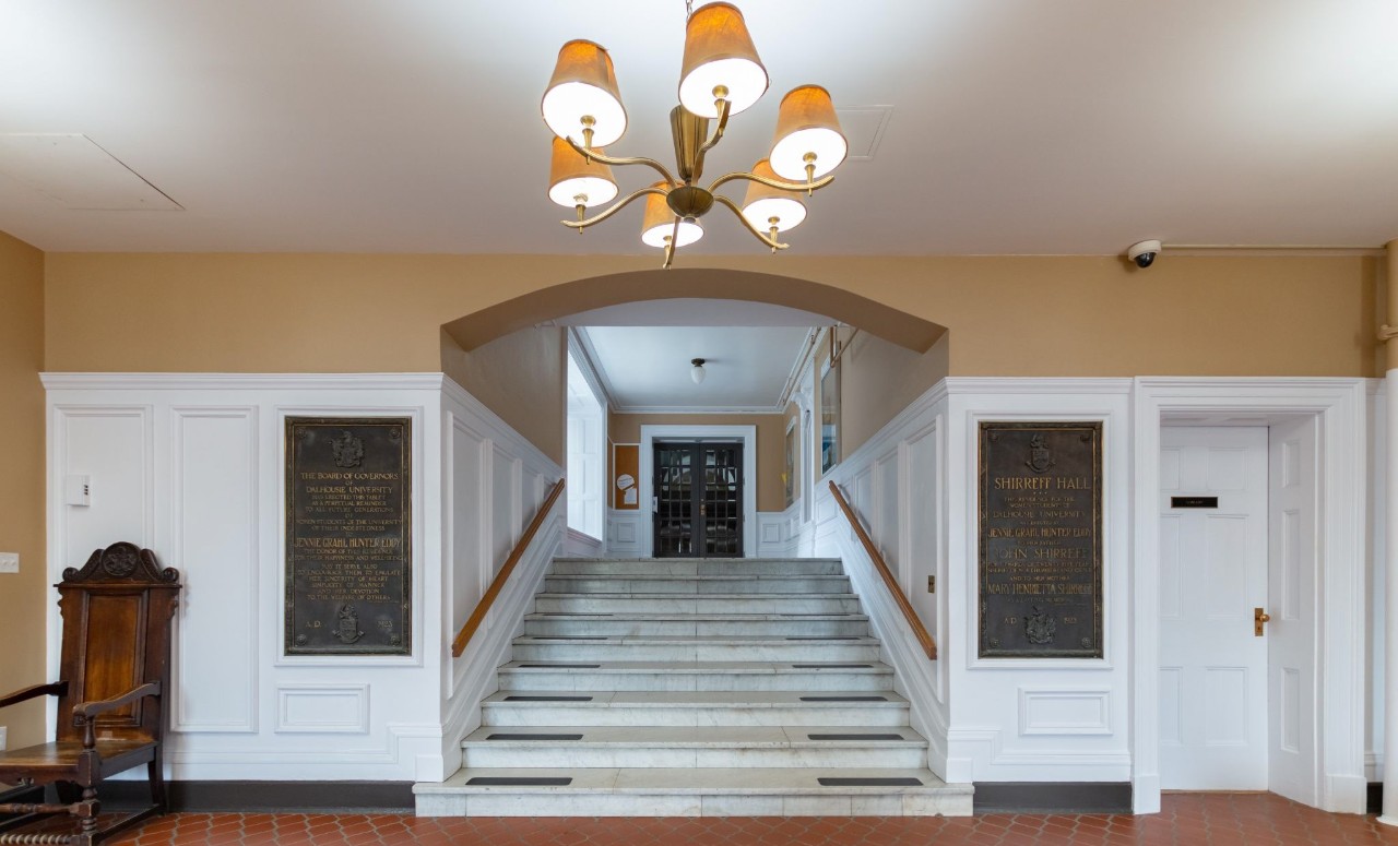 The Lobby of Shirreff Hall, featuring a chandelier, large wooden chair, marble stairs and terracotta tile floor.