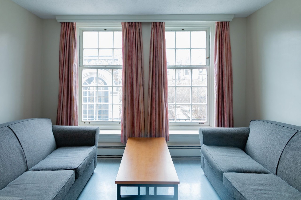 A small lounge in New Eddy house, featuring grey fabric sofas and a coffee table, with large windows.