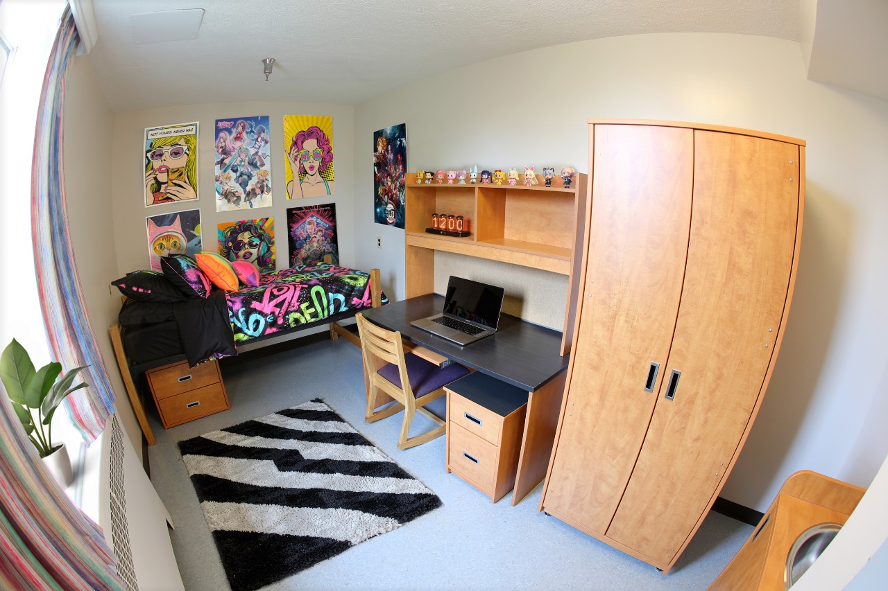 A single room in New Eddy in Shirreff Hall, staged with bedding, a laptop on the desk, and posters on the wall.