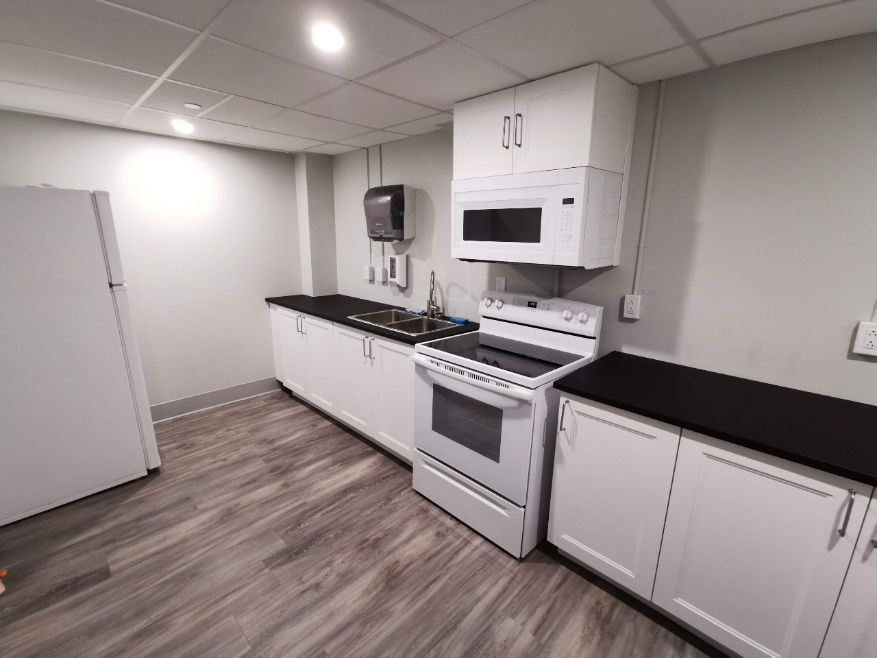 The full kitchen in New Eddy's basement lounge is modern, with white cupboards and black counters, and offers a stove and oven, fridge, sink, and microwave.