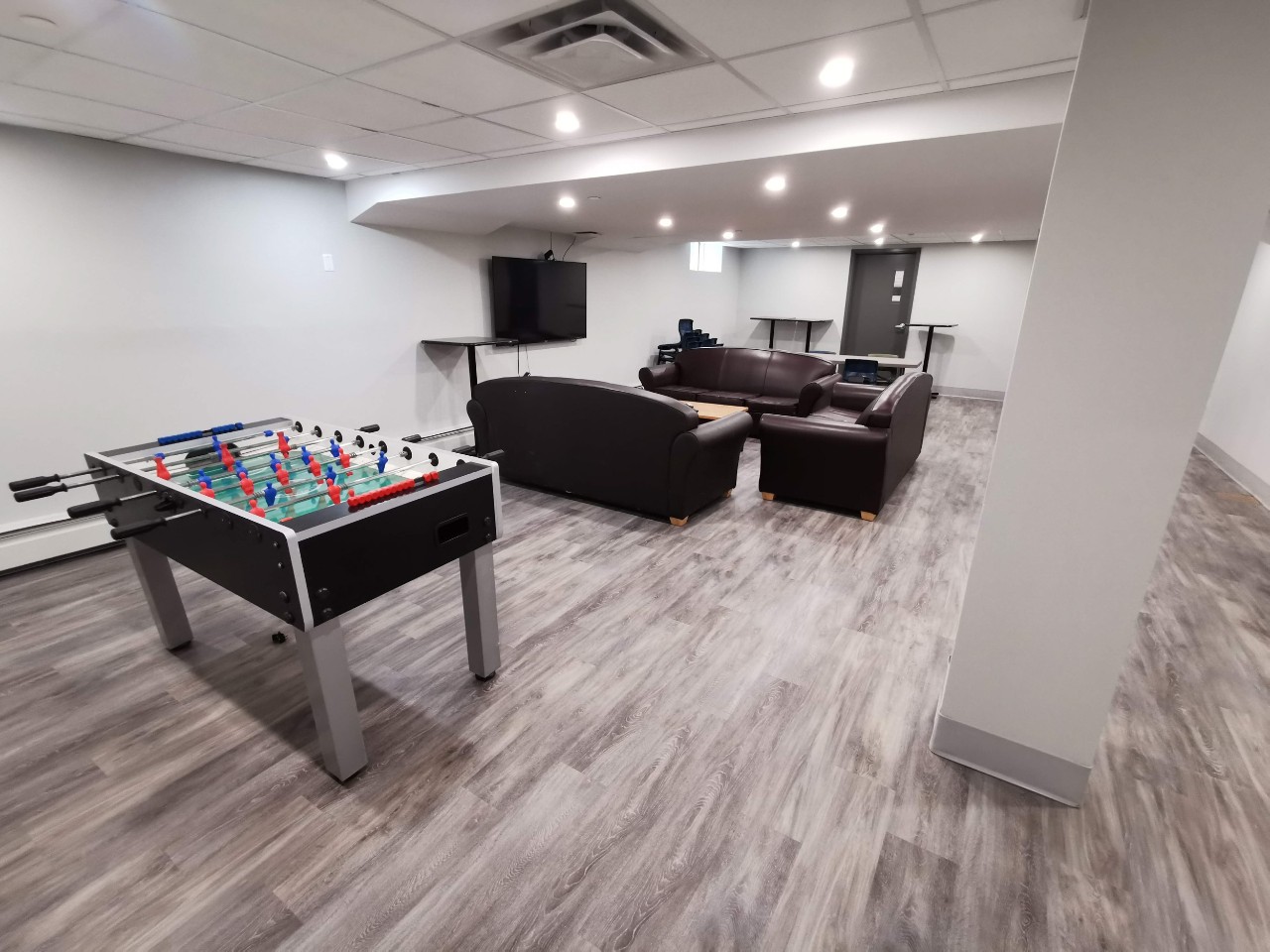 The newly renovated lounge has modern grey floors, dark sofas, and a foosball table.
