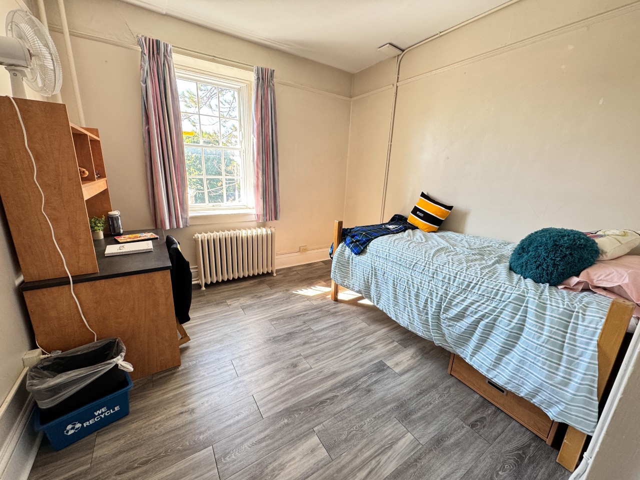 The single room has plenty of open space, a desk, bed, and built-in closet, with a large bright window.